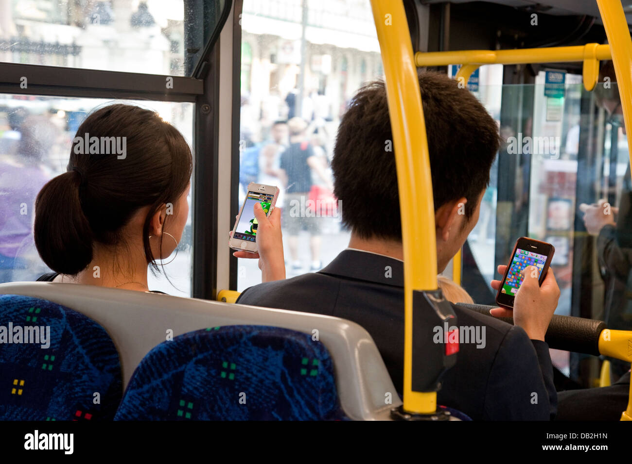 Zwei Menschen sitzen auf einem Londoner Bus Spiel Candy Crush Saga auf ihren Iphones, London, England Stockfoto