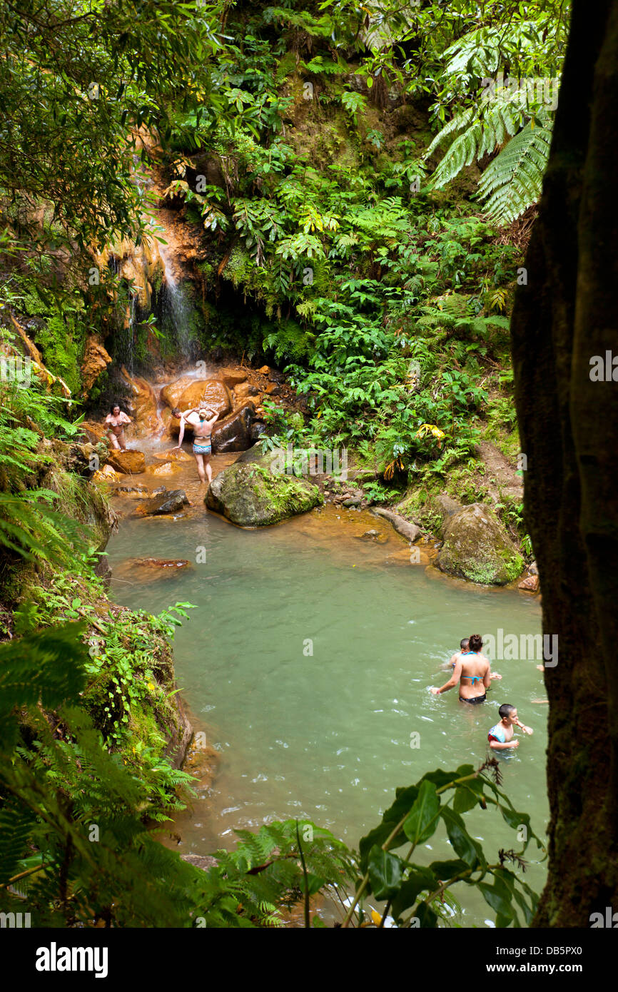 Bei Caldeira Velha sind Menschen in einem Pool mit warmem Wasser aus einem Wasserfall baden. Stockfoto
