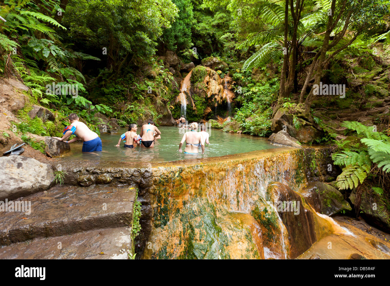 Bei Caldeira Velha sind Menschen in einem Pool mit warmem Wasser aus einem Wasserfall baden. Stockfoto