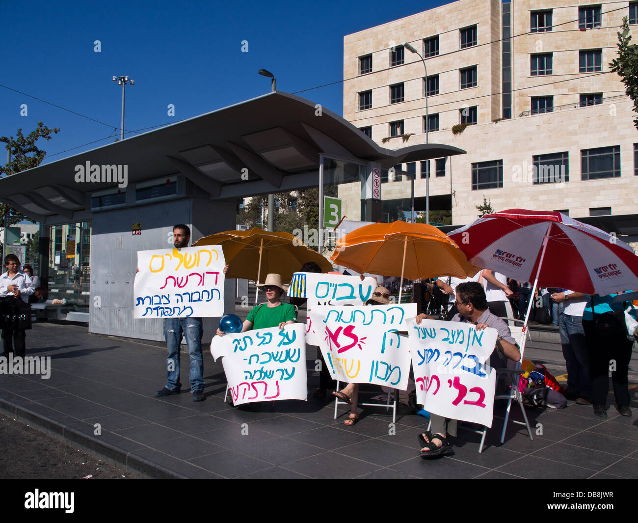 Jerusalem, Israel. 25. Juli 2013. Ausgestattet mit bunten Sonnenschirmen und Zeichen, eine Handvoll Aktivisten inszenieren eine Beach Party Demonstration gegen die öffentlichen Verkehrsmittel der Stadt. Jerusalem, Israel. 25. Juli 2013. Eine Handvoll Aktivisten inszenieren eine "Strand Party Demonstration" gegen das öffentliche Transportsystem Stadt anhand der Light Rail Transit (Tram) und Busse, behauptet überfüllten Busse und Züge, Verspätungen, Unregelmäßigkeit und Armen Tierheim an den Haltestellen. Bildnachweis: Nir Alon/Alamy Live-Nachrichten Stockfoto