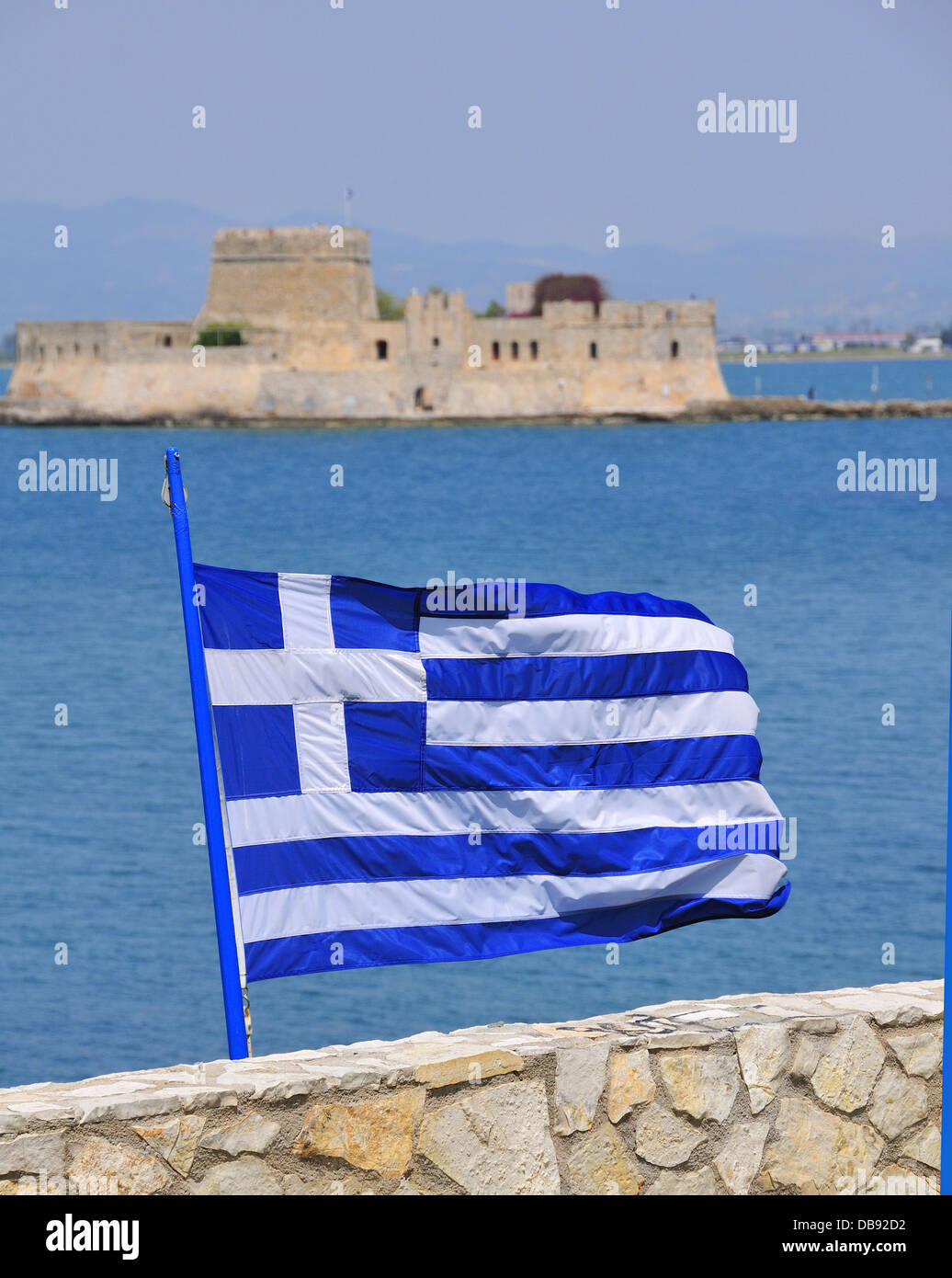 Griechische Flagge in der Küstenstadt Nafplion mit der Venezianischen Burg Bourtzi in der Mitte des Hafens im Hintergrund Peloponnes, Griechenland fliegen Stockfoto