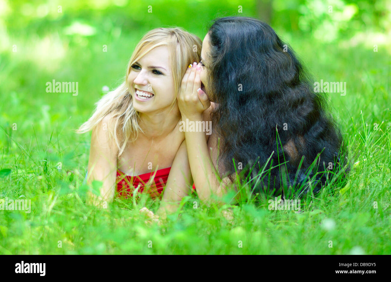 zwei flüsternde Freundinnen liegen auf dem Rasen Stockfoto