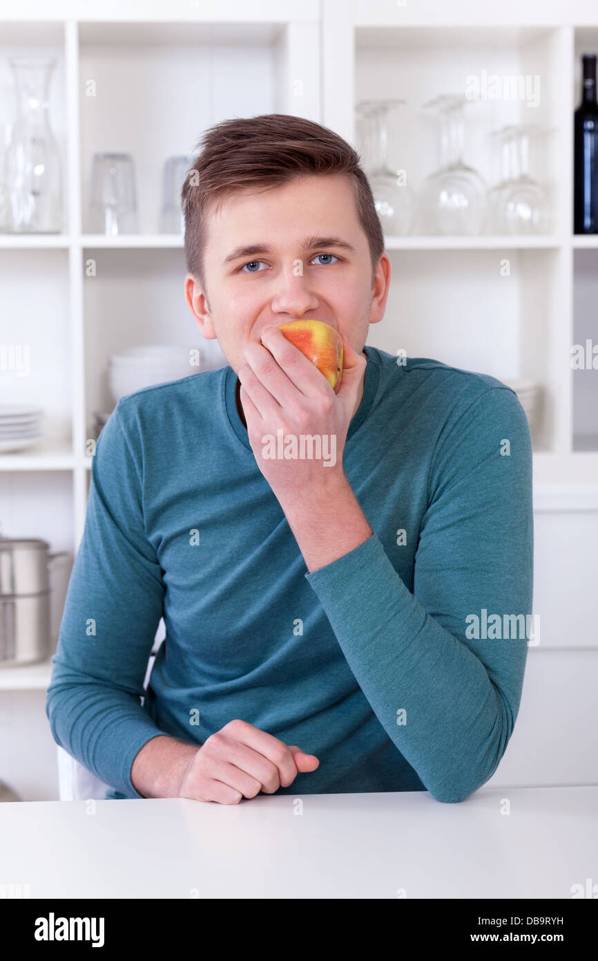 junger Mann in seiner modernen Küche einen gesunden Apfel essen Stockfoto