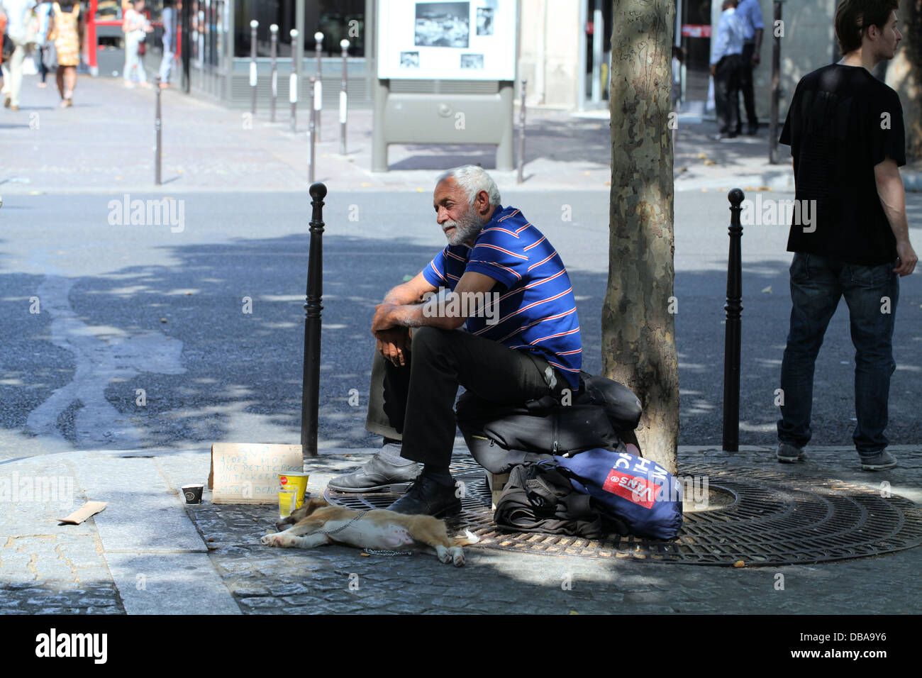 Ein Obdachloser Mann sitzt im Schatten unter einem Baum mit seinem Hund in Paris, Frankreich Stockfoto