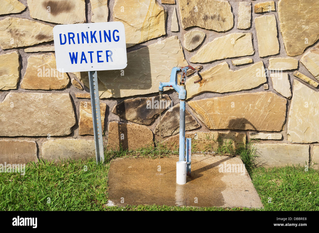 Trinkwasserhahn mit Zeichen und fließendem Wasser hinter einer Steinmauer Stockfoto