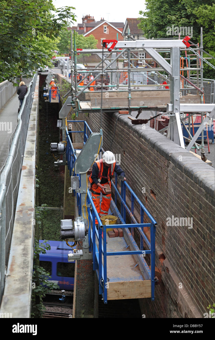Arbeiter zu renovieren die gemauerte Brüstung mit einer Straßenbrücke über eine Bahnstrecke mit abgehängten Hubarbeitsbühnen. Ein Zug geht unter. Stockfoto