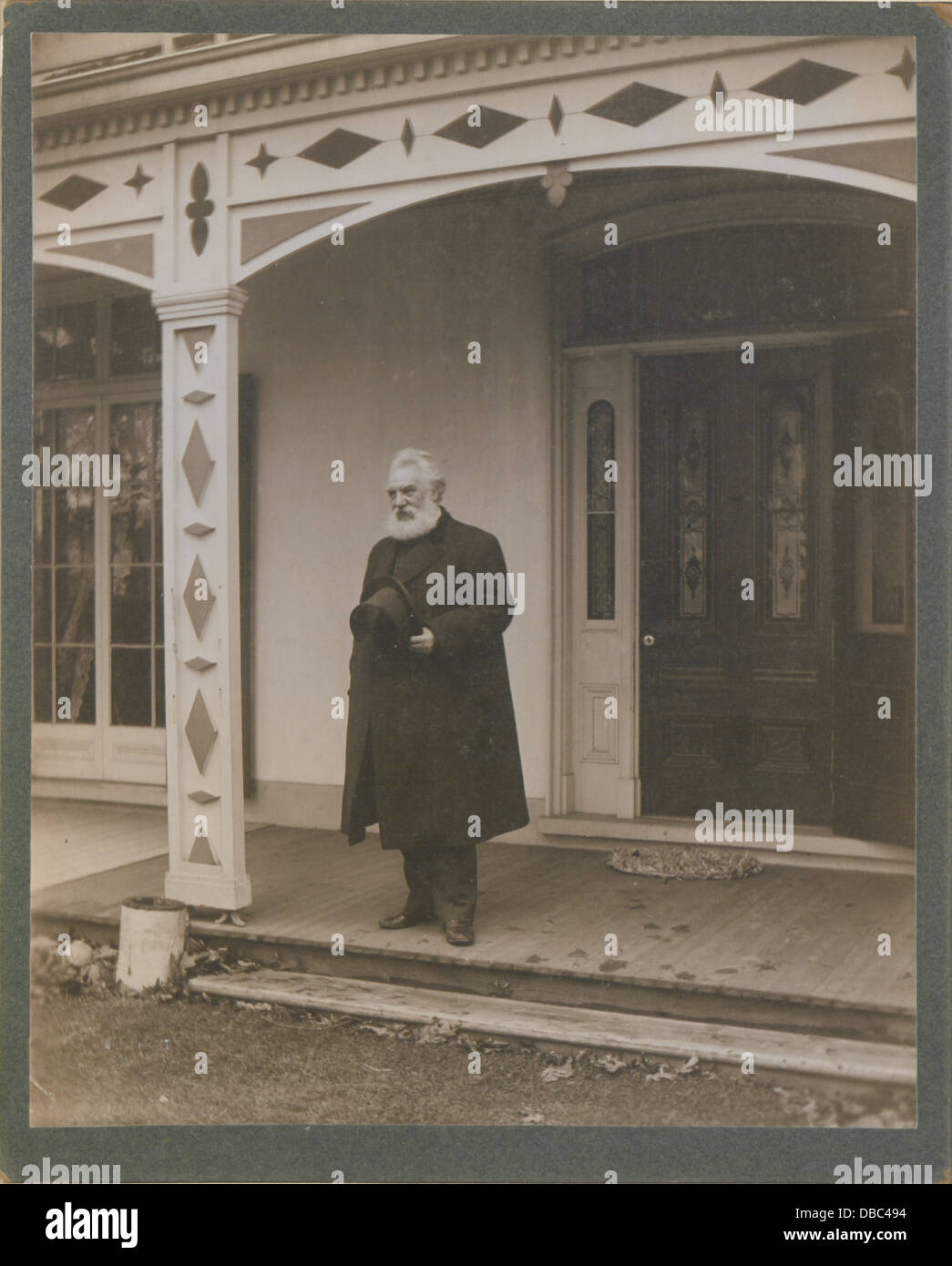 Dieses historische Foto zeigt Alexander Graham Bell, der an der Tür seines Hauses steht, mit seiner Erfindung des Telefons im Hintergrund, was einen entscheidenden Moment in der Kommunikationsgeschichte markiert. Stockfoto