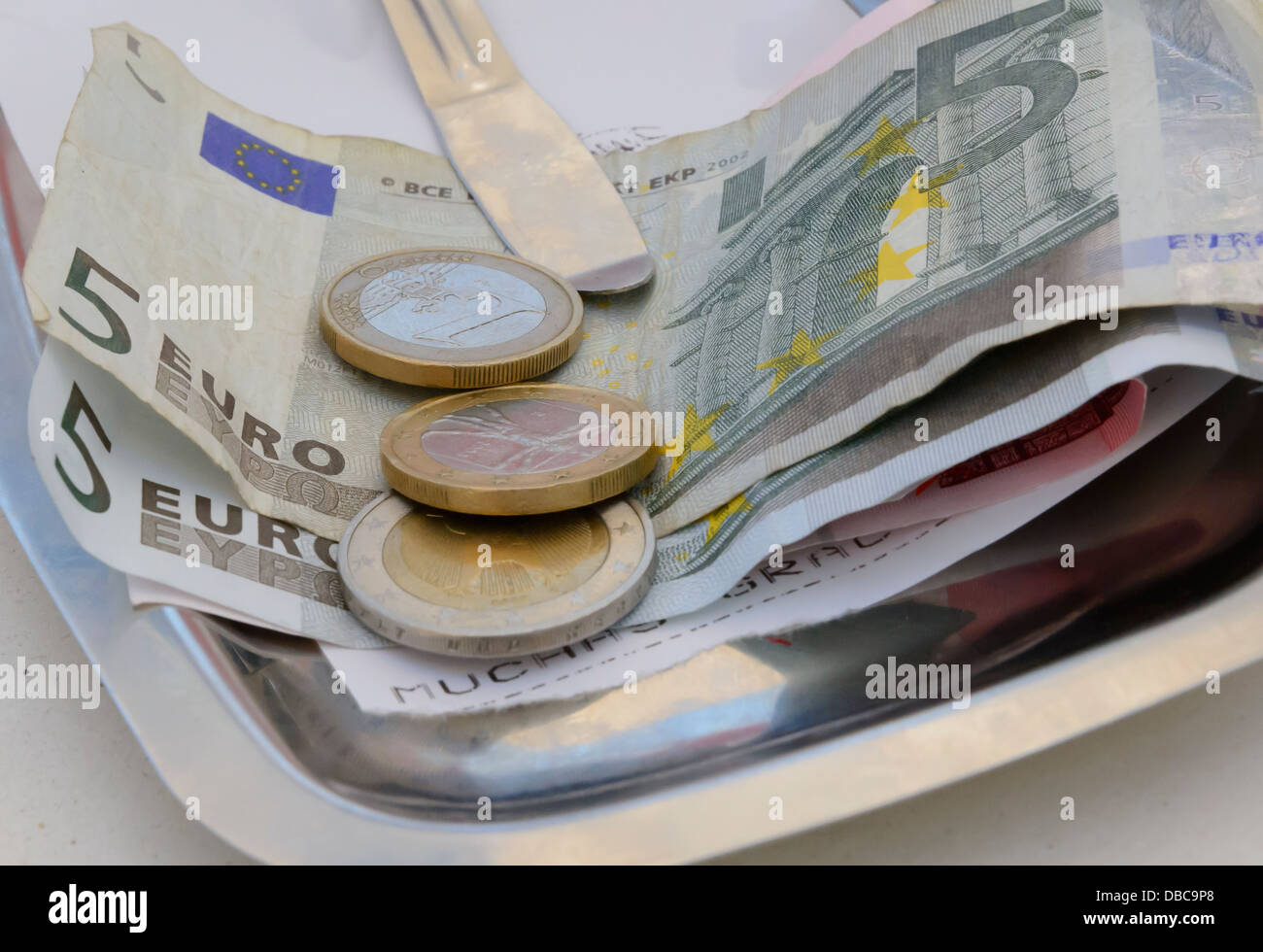Rechnungen von fünf Euro und Münzen als Zahlungsmittel im Restaurant und eine Rechnung mit "Muchas Gracias". Stockfoto
