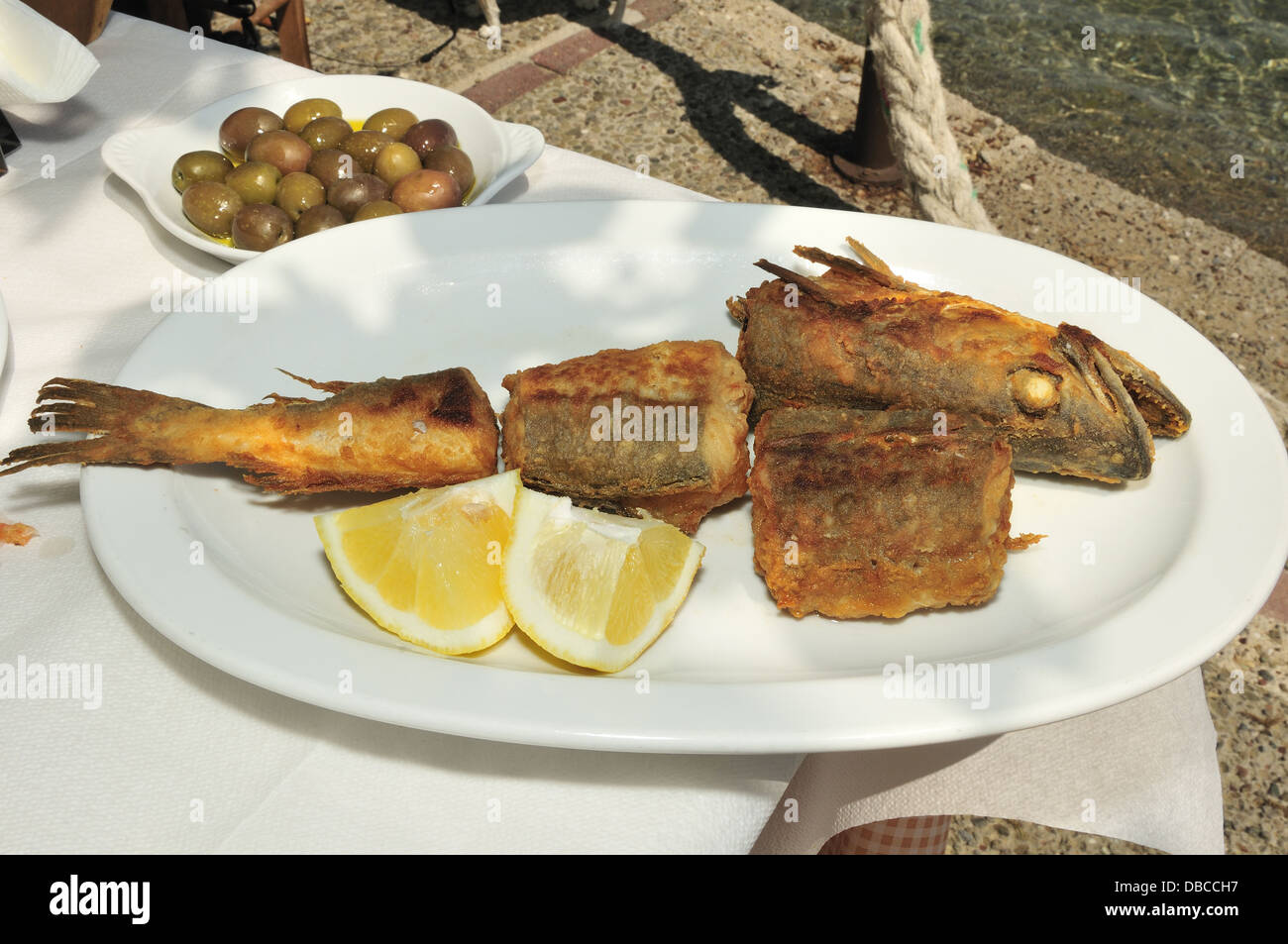 Restaurant am Wasser mit Kabeljau in Mehl gebraten und in Olivenöl mit Zitrone und Gericht von Oliven in Gikes, Peloponnes, Griechenland gekocht Stockfoto