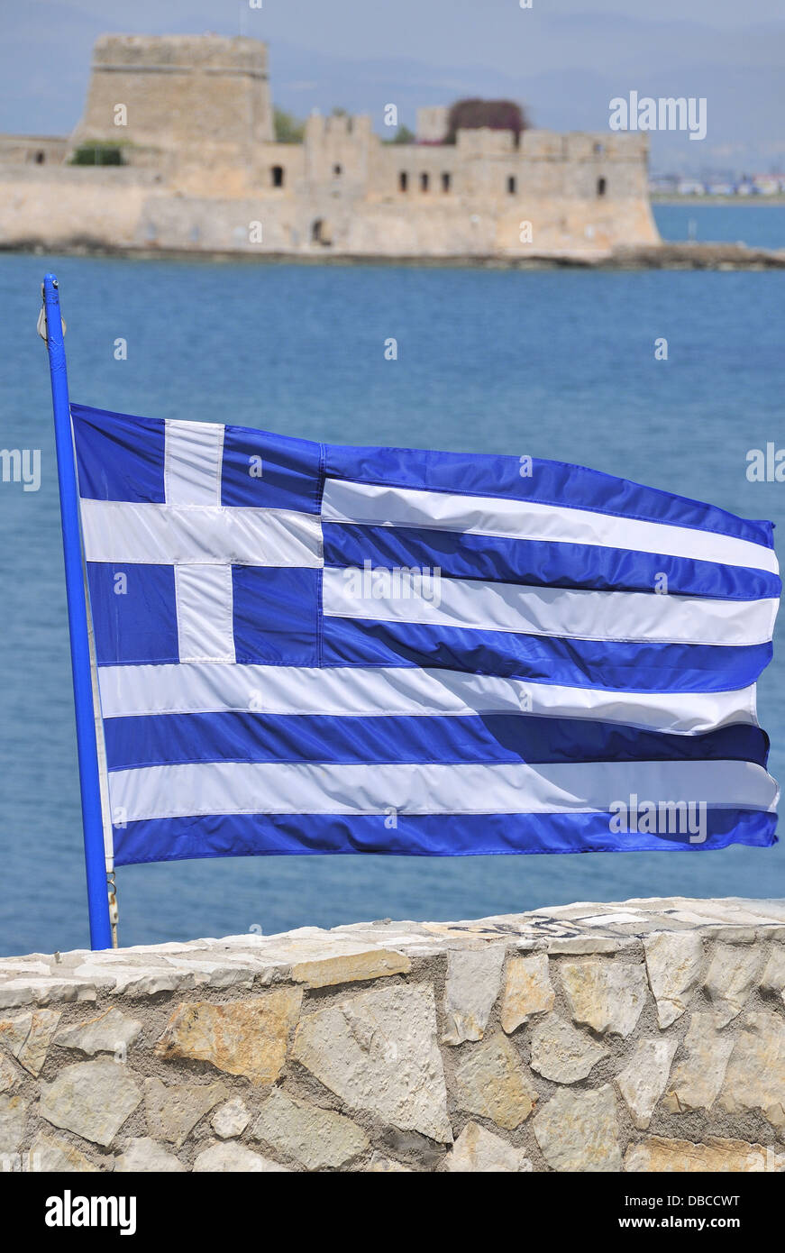 Griechische Flagge in der Küstenstadt Nafplion mit der Venezianischen Burg Bourtzi in der Mitte des Hafens im Hintergrund Peloponnes, Griechenland fliegen Stockfoto