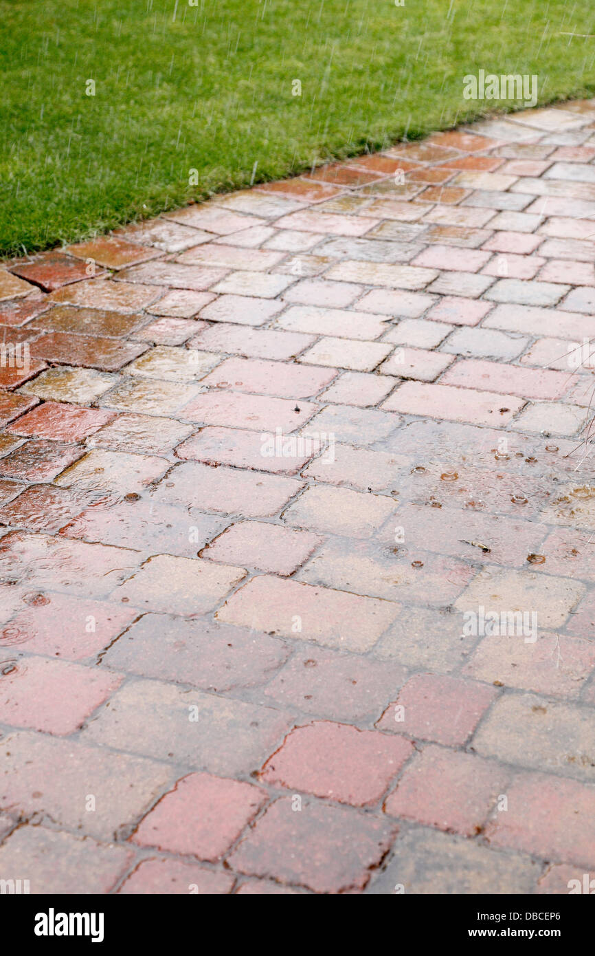 Schwere Regentropfen auf rustikalen aus rotem Backstein Innenhof Pflasterung in UK Garten mit porösen Fugen als Oberflächenwasser Sickerschacht spritzt Stockfoto
