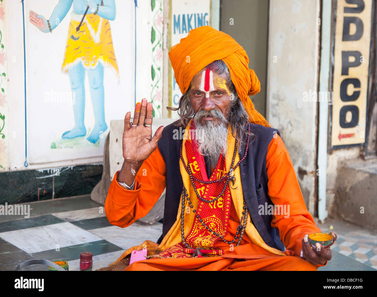 Ein älterer bärtiger Hindu Sadhu, heiliger Mann, in traditionellen bunten Safran Roben, einen Segen in Udaipur, Indien im Gegenzug für Almosen geben Stockfoto