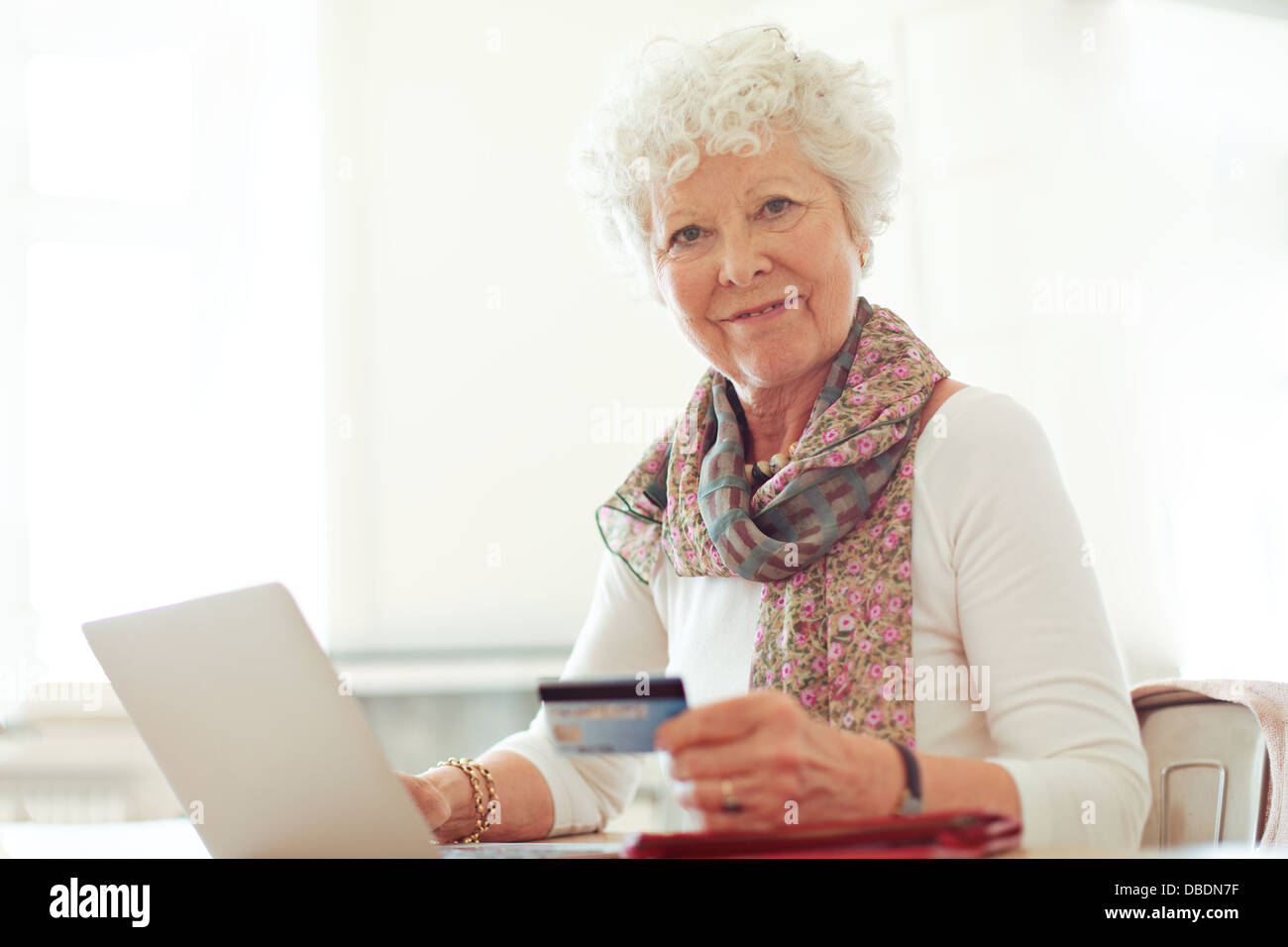 Reife Dame mit einer Kreditkarte vor ihrem Laptop lächelnd Stockfoto