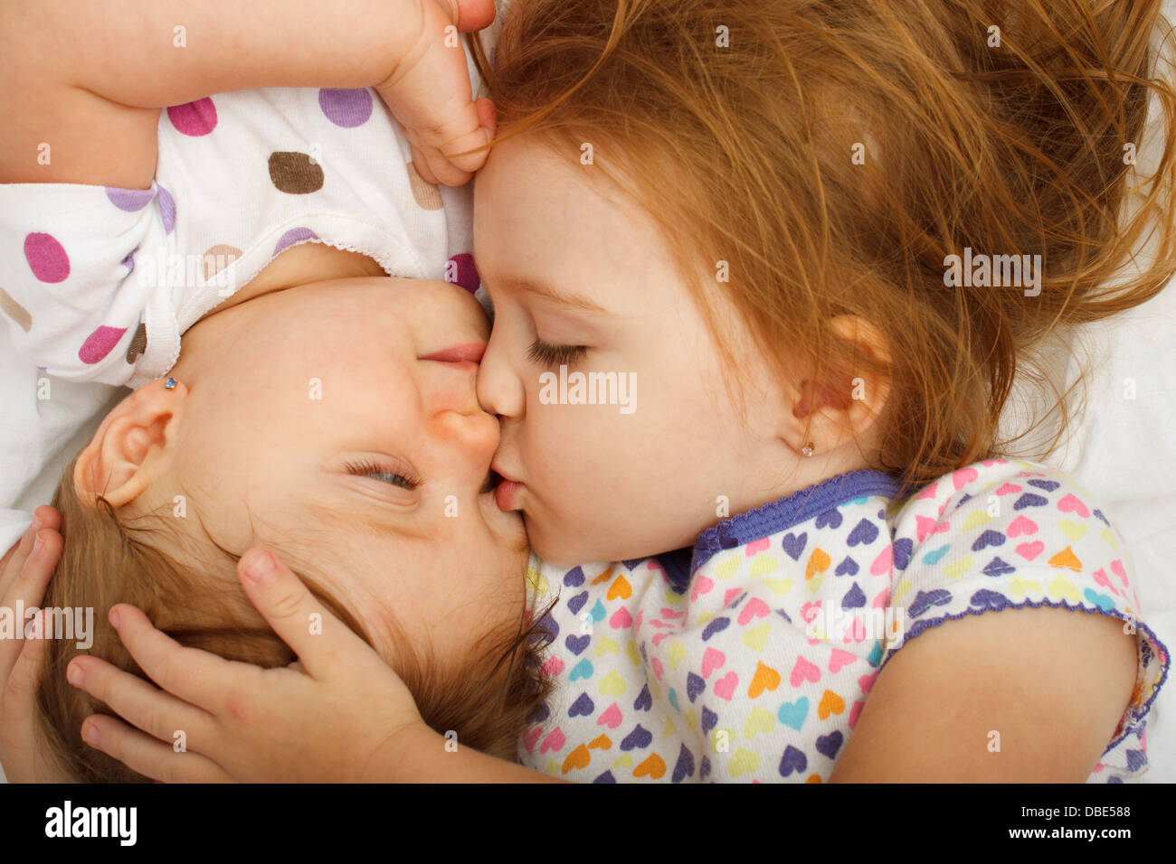 Ältere Schwester küssen Baby im Bett Stockfoto