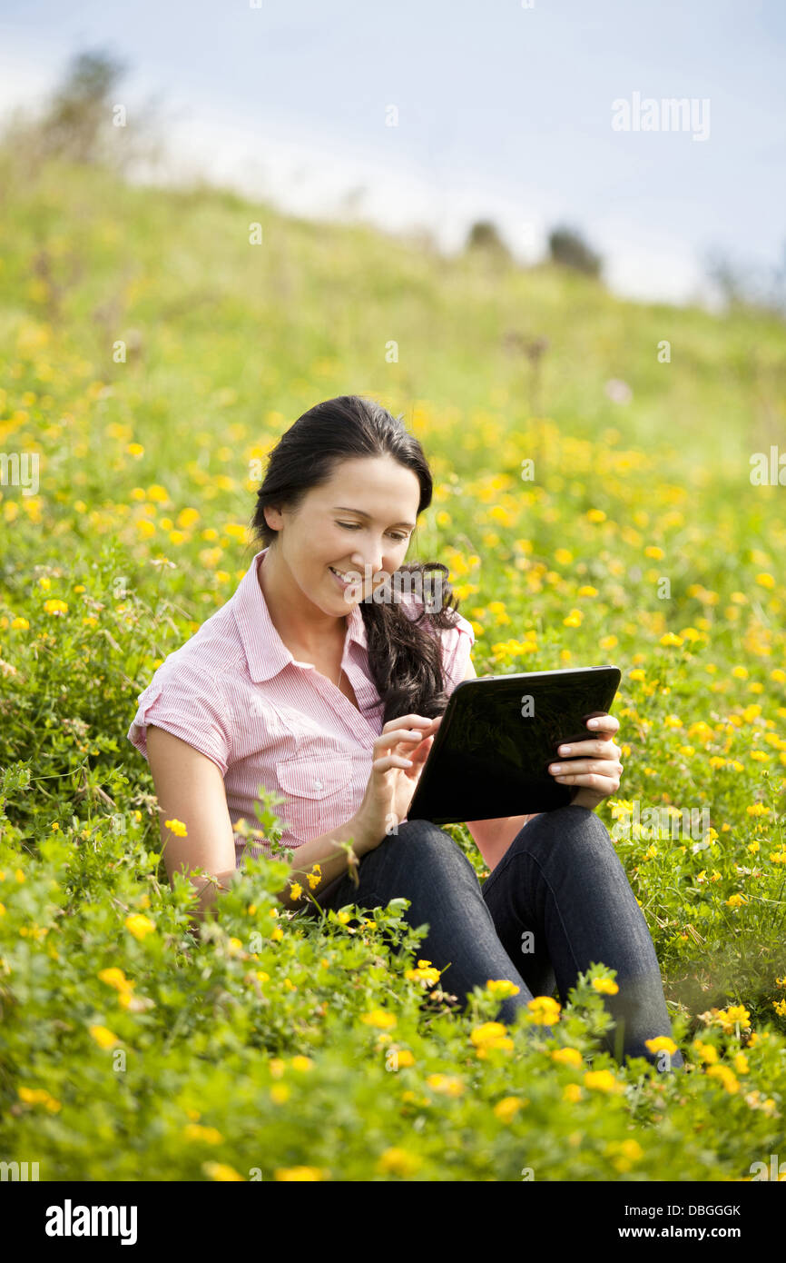 Junge dunkelhaarige Mädchen sitzen auf einer Wiese und mit einem Tablet-PC Stockfoto