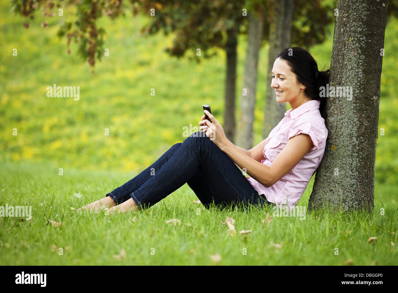 Junge dunkelhaarige Mädchen an einen Baum gelehnt und mit einem mobilen Stockfoto