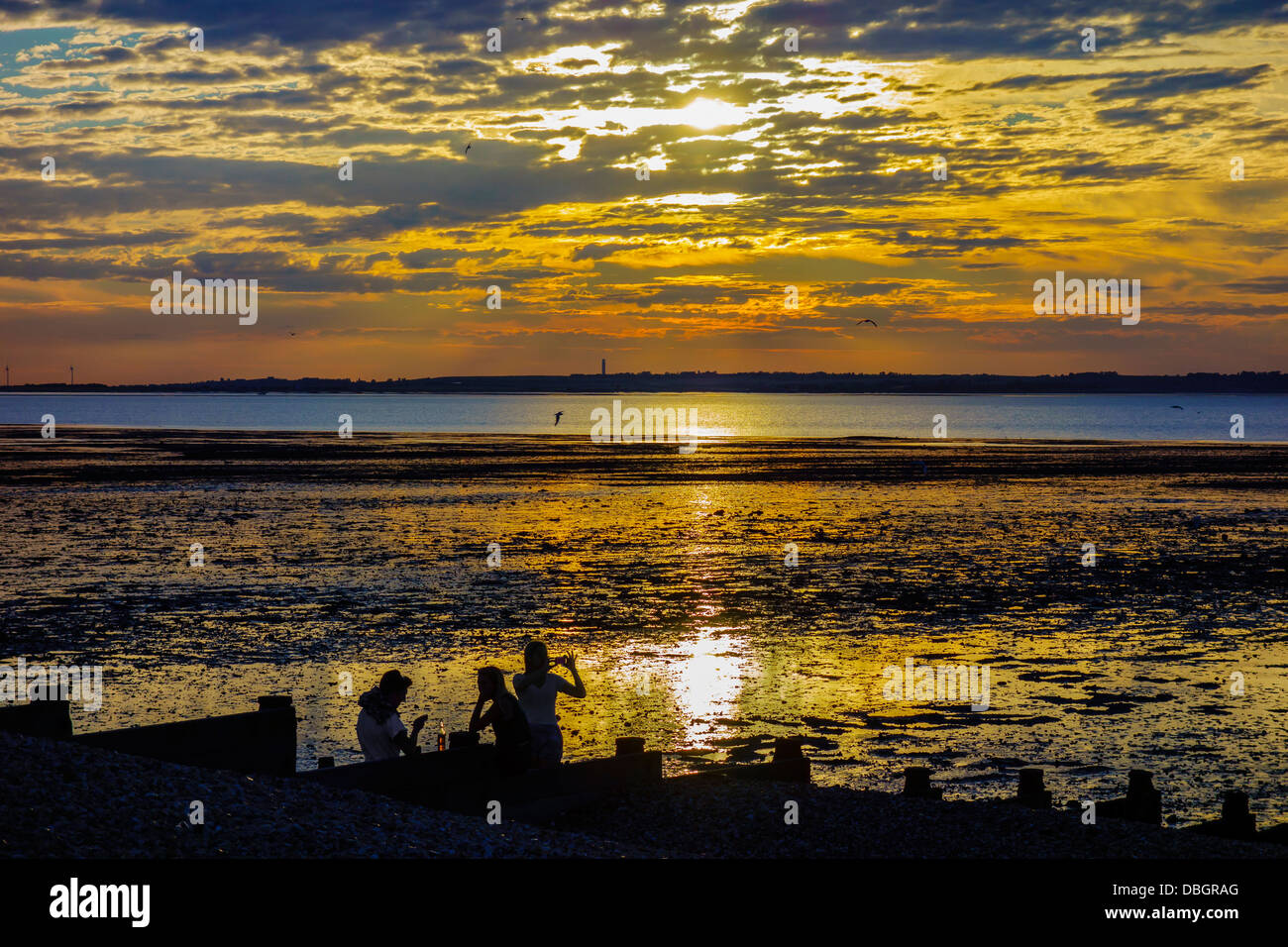 Menschen, die einen Drink bei Sonnenuntergang am Strand von Whitstable Kent Stockfoto