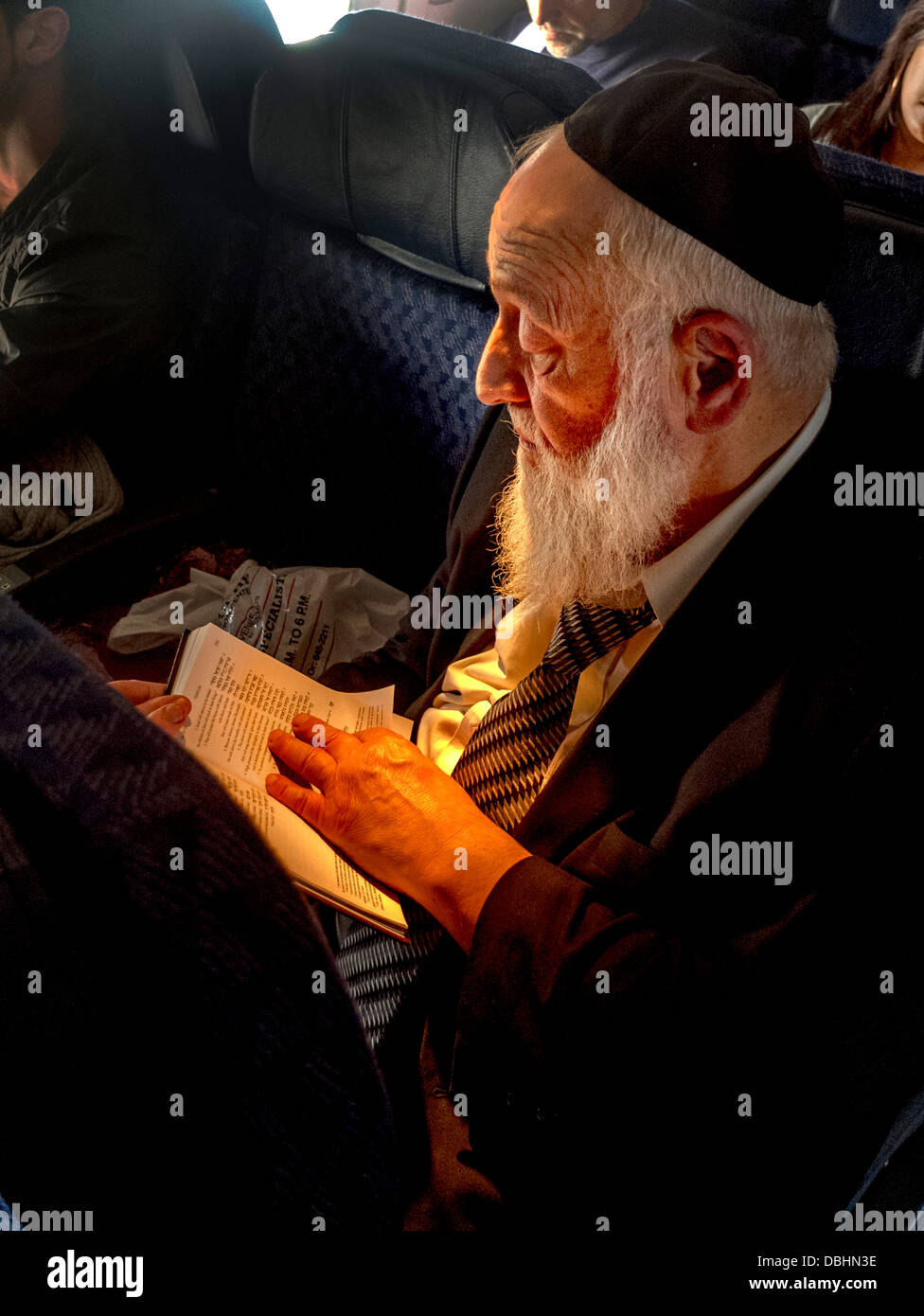 Tragen eine Kippa Käppchen, liest ein bärtiger orthodoxer Jude aus einem Buch auf Hebräisch auf ein Verkehrsflugzeug Stockfoto