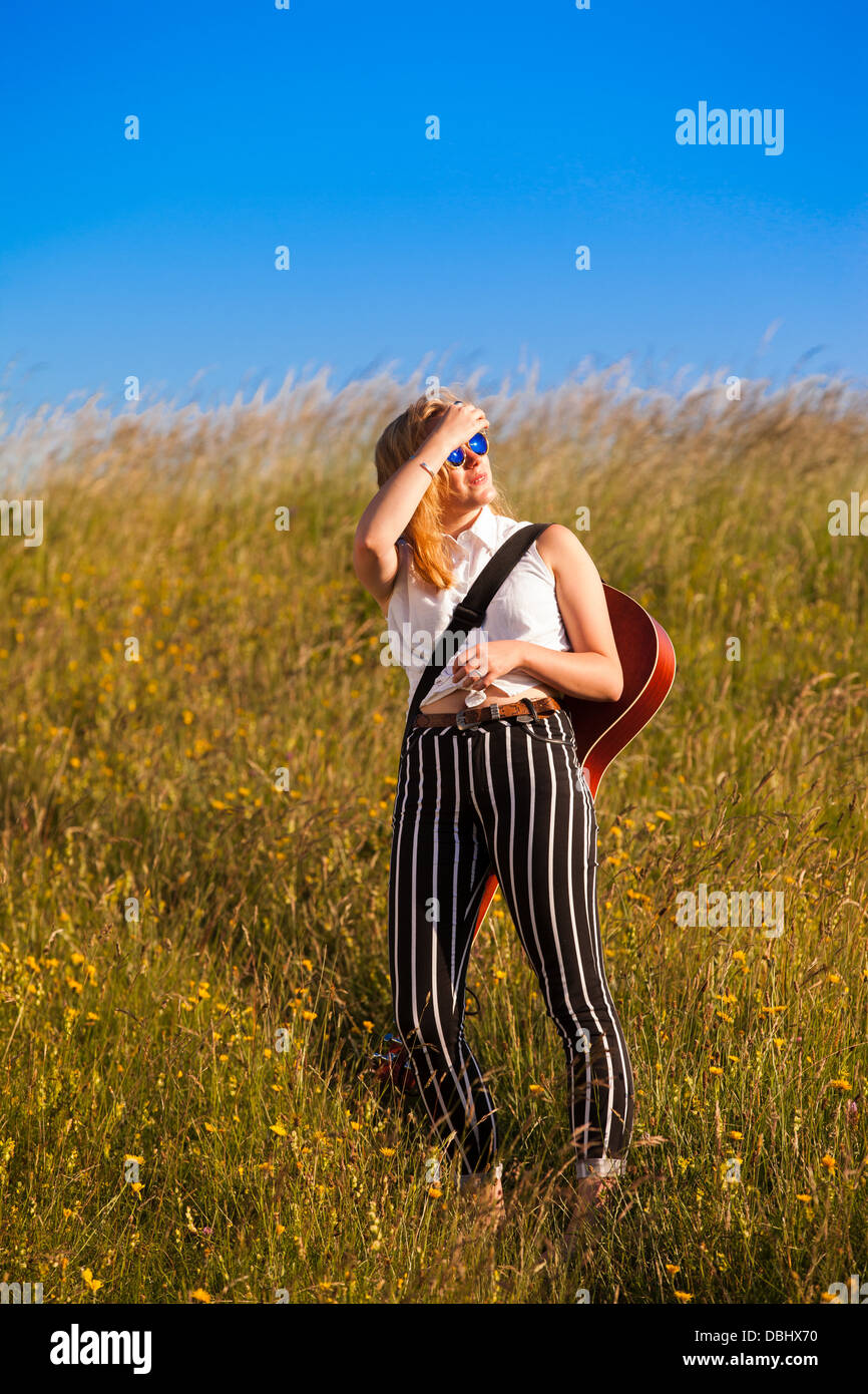 Teenager-Mädchen zu Fuß durch eine Wiese mit einer Gitarre. Im Freien. Sommer. Stockfoto