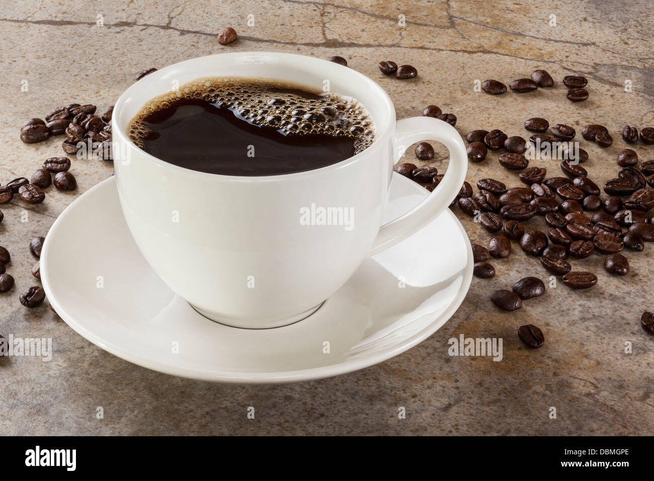 Tasse Kaffee auf einem oberen Marmortisch mit Kaffeebohnen verstreut. Von vorne nach hinten Fokus. Stockfoto