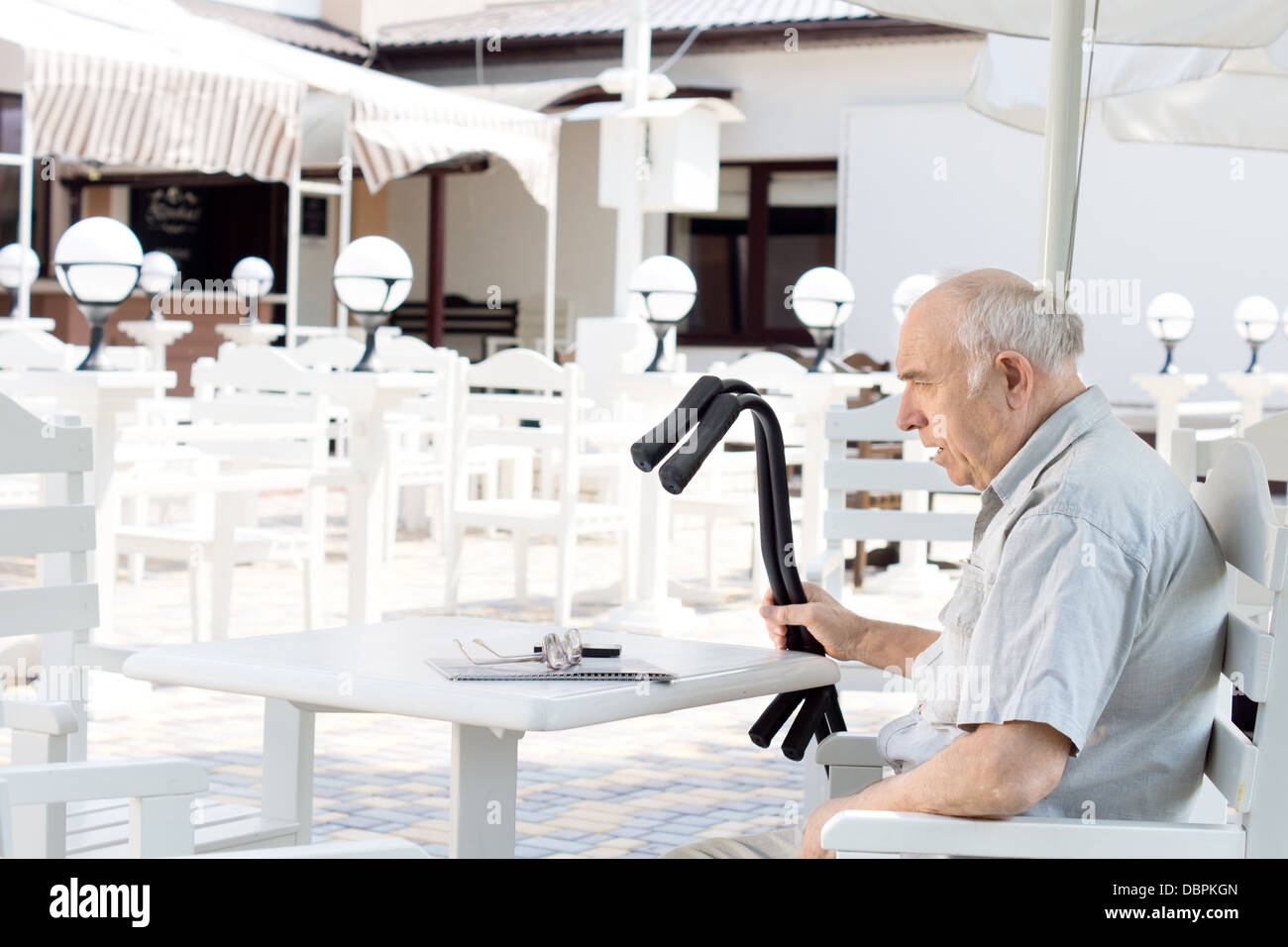 Senioren Behinderte Mann mit Krücken saß allein an einem Tisch in einem Restaurant im freien Stockfoto