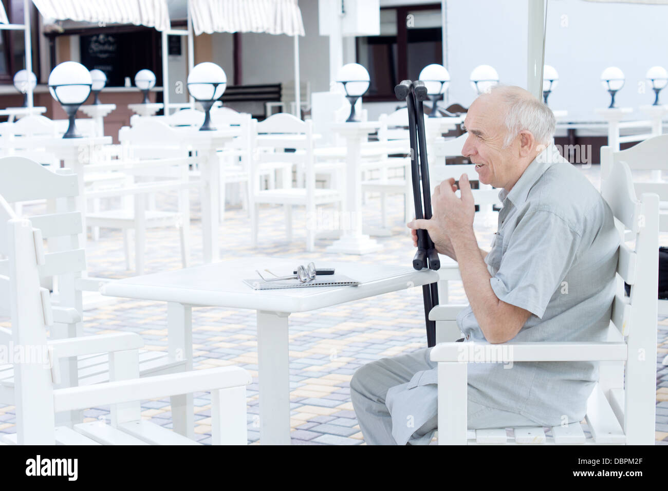 Ältere Amputierte sitzen an einem Tisch im Restaurant im freien seine Krücken in der Hand halten, wie er auf seine Begleiter wartet kommen Stockfoto