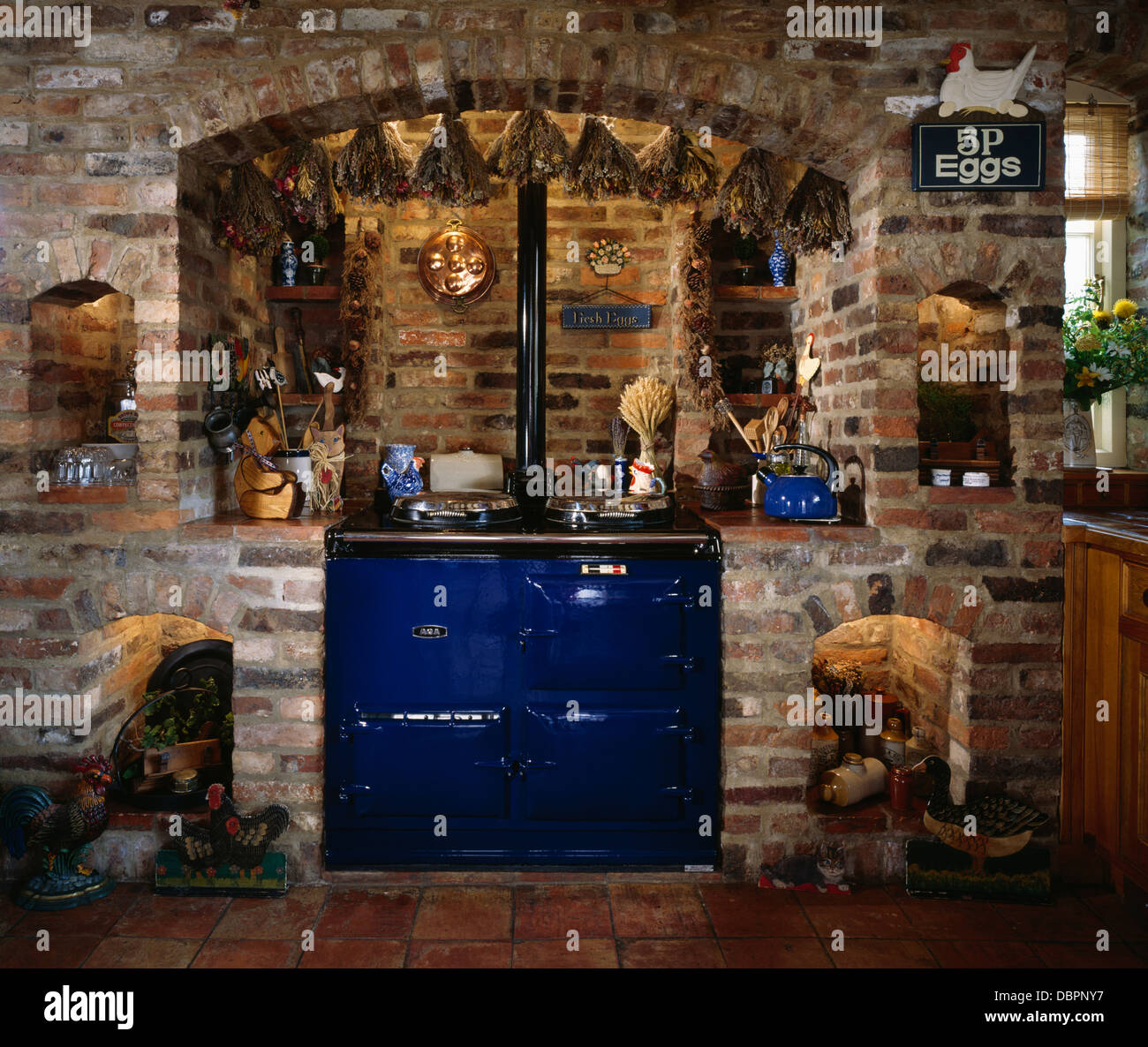 Trauben von getrockneten Blüten hängen oben blau Aga in Backstein Wand im Cottage-Küche Stockfoto