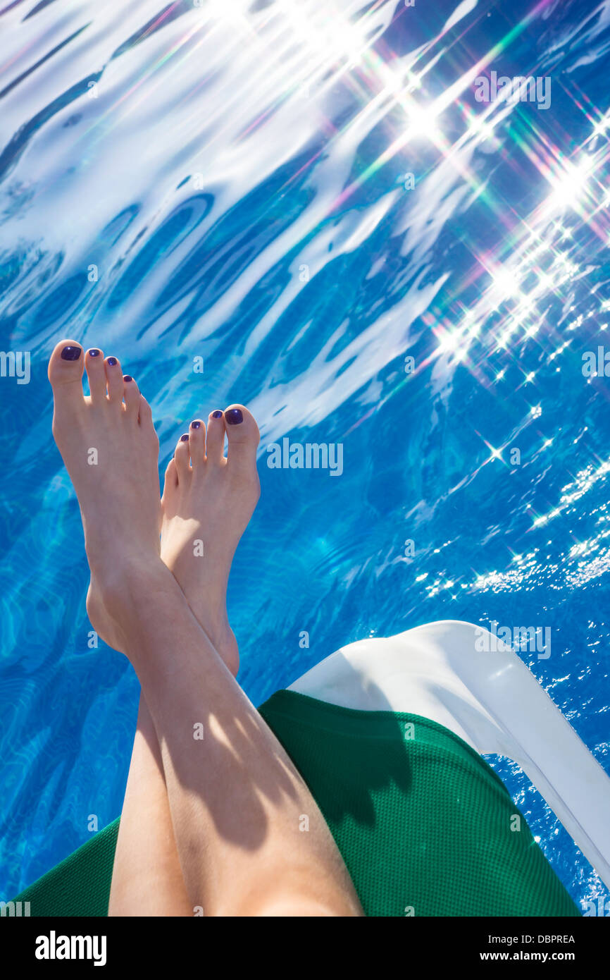 Eine junge Frau entspannt sich mit ihren Füßen bis auf eine Sonnenliege am Pool. Stockfoto