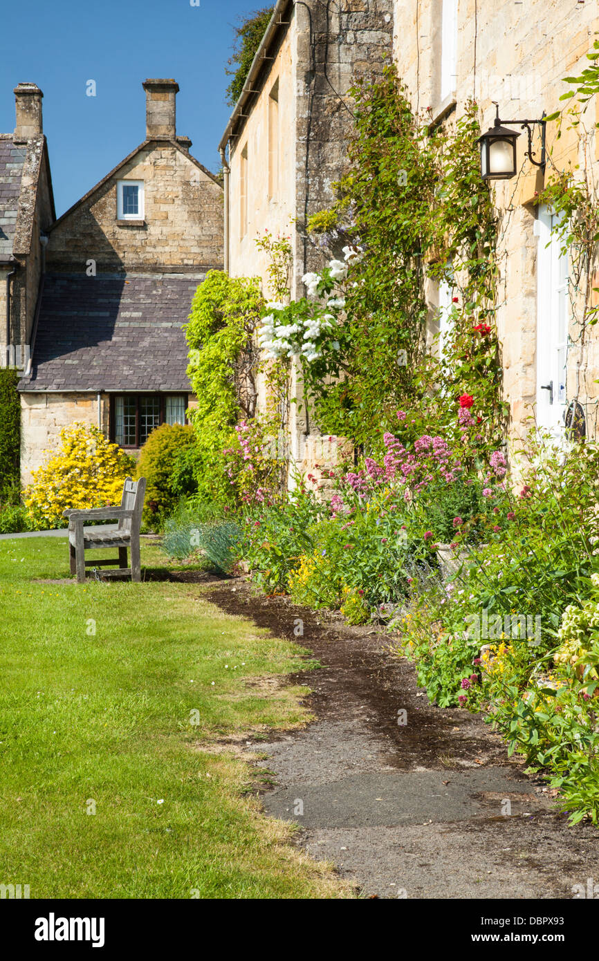 Honig-gesteinigt Cotswold Hütten mit Rosen und Sommerblumen, neben den Dorfanger in Stanton, Cotswolds, Gloucestershire, England Stockfoto