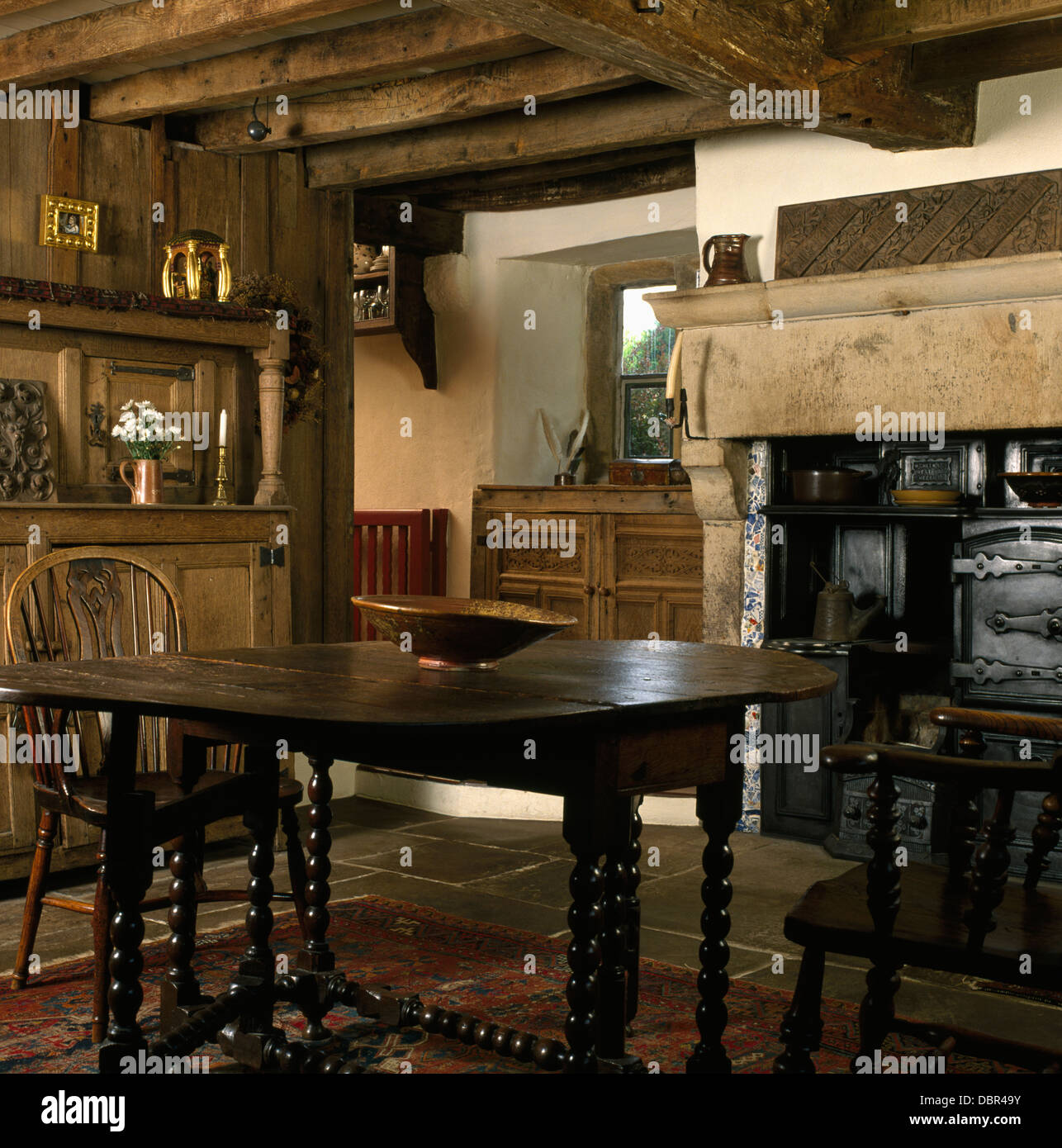 Windsor Stühle und jakobinischen Eichentisch mit Gerste-Twist Beinen in Holzbalken Land Esszimmer mit alten gusseisernen Kamin Stockfoto