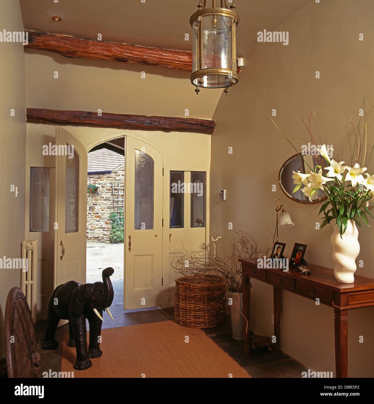 Vase mit weißen Lilien auf Konsoltisch im Land Saal mit hölzerner Elefant neben Hälfte verglasten Front Tür öffnen Stockfoto