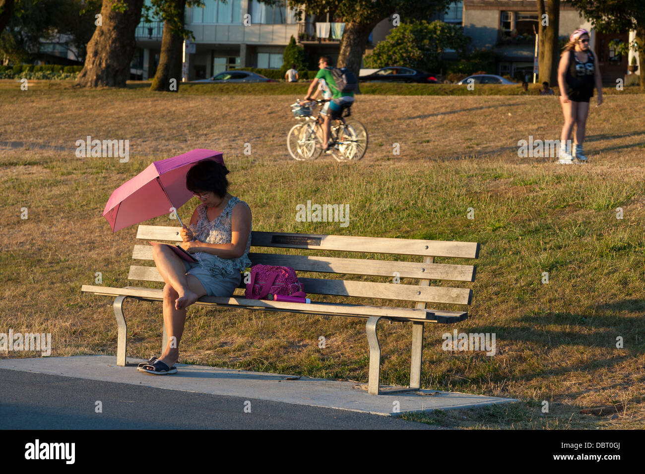 Frau liest im Schatten eines Sonnenschirms entlang Sunset Beach Park - Westend, Vancouver, Britisch-Kolumbien, Kanada Stockfoto