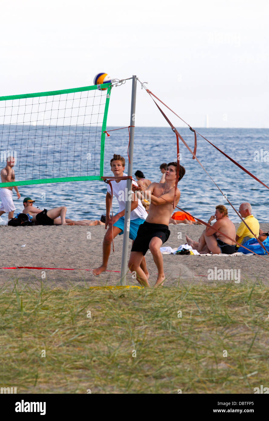 Teenager am Strand spielen Strandvolley für den Spaß an einem heißen und sonnigen Sommernachmittag an der Küste von Øresund. Dänische Hyge. Stockfoto