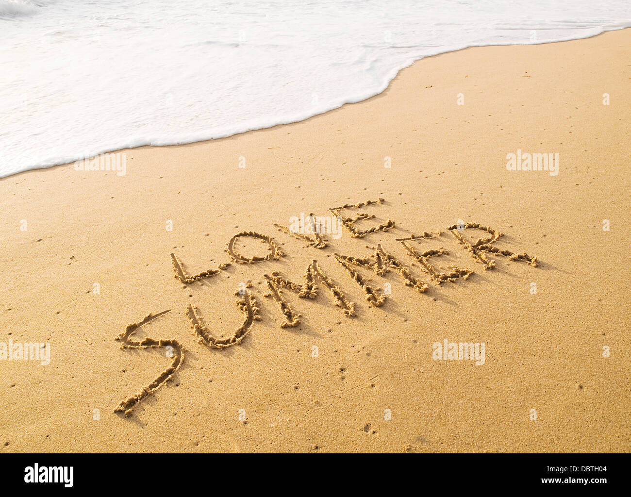 Text "Liebe Sommer" im Sand am Strand mit einer Welle geschrieben. Stockfoto