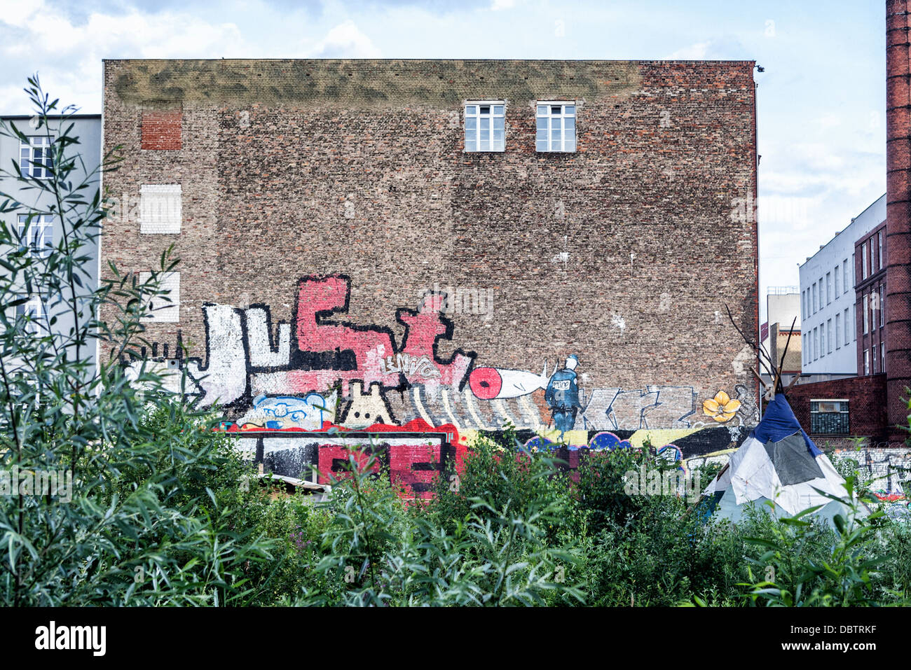 Die Graffiti bedeckt Wand eines Gebäudes mit ein Hausbesetzer Zelt im Vordergrund - Cuvrystrasse, Kreuzberg, Berlin Stockfoto