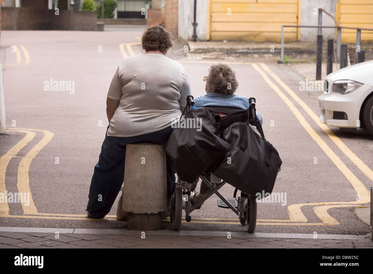 Zwei Damen sitzen geduldig, auf doppelte gelbe Linien für einen Aufzug warten. Stockfoto
