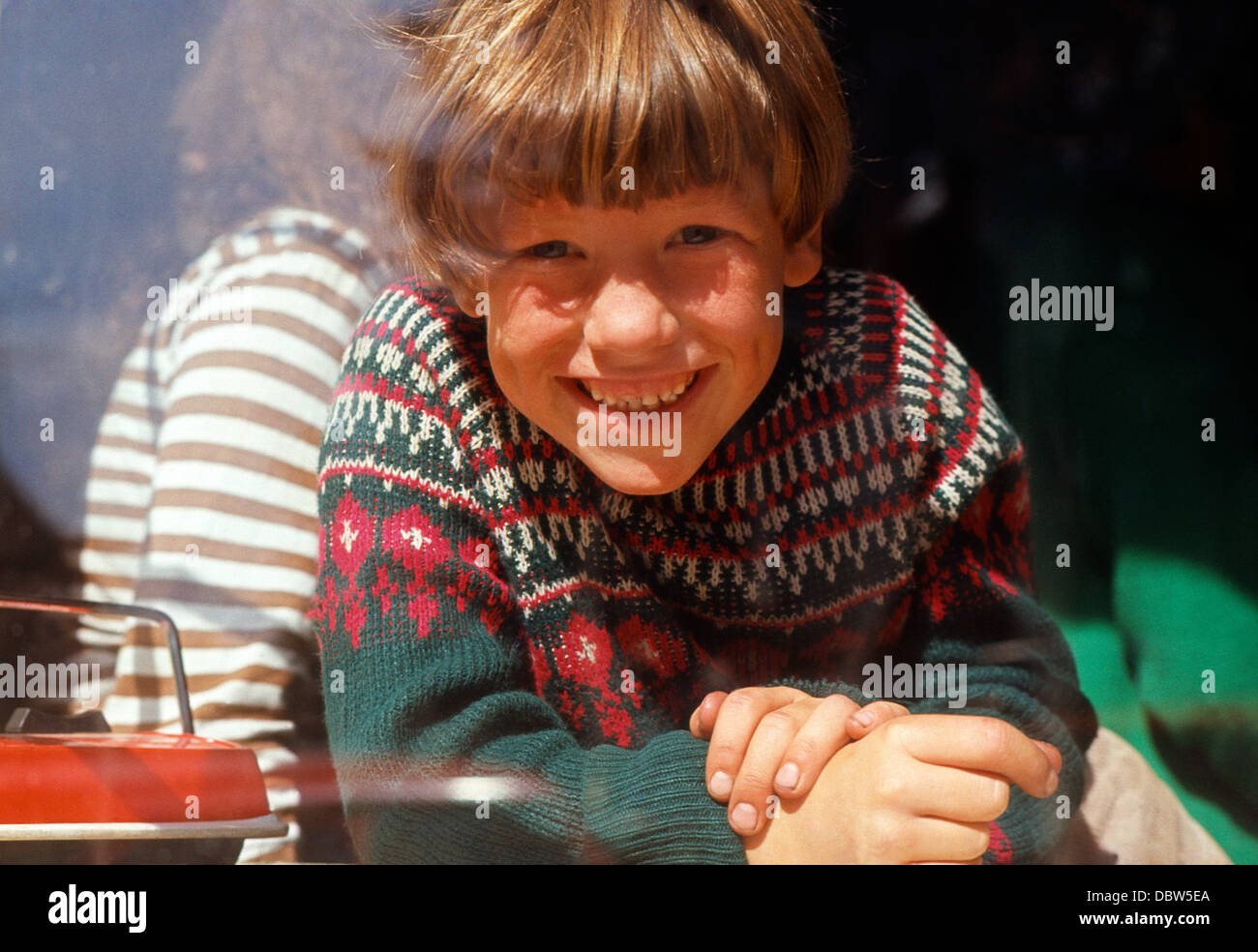 Kleiner Junge lächelt der Kamera zu und schaut durch ein Fenster in den 1970er Jahren Norfolk UK England Großbritannien in den 1970er Jahren 1973 KATHY DEWITT Stockfoto