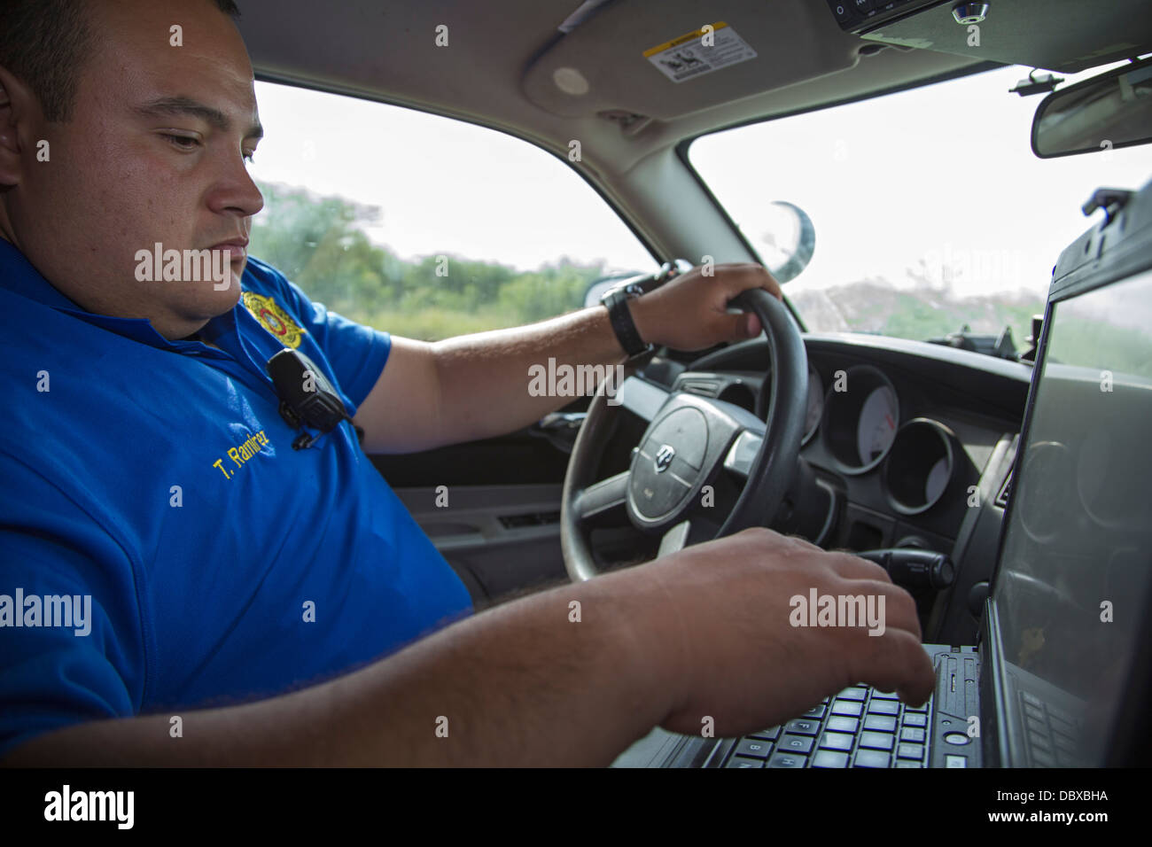 Brooks County, Texas Hilfssheriff Tomas Ramirez gibt Daten auf seinem Streifenwagen Computer während der Fahrt eine Kreisstraße. Stockfoto