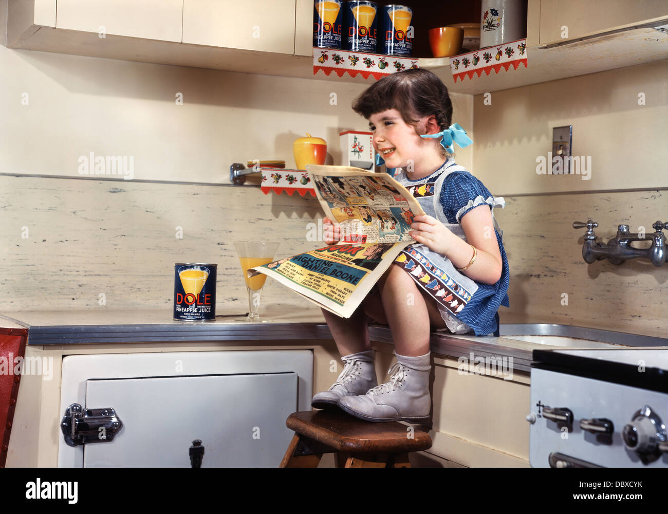 1950ER JAHREN LÄCHELNDE MÄDCHEN SITZEN AUF KÜCHE ZÄHLER LESEN SONNTAG COMICS FUNNIES Stockfoto