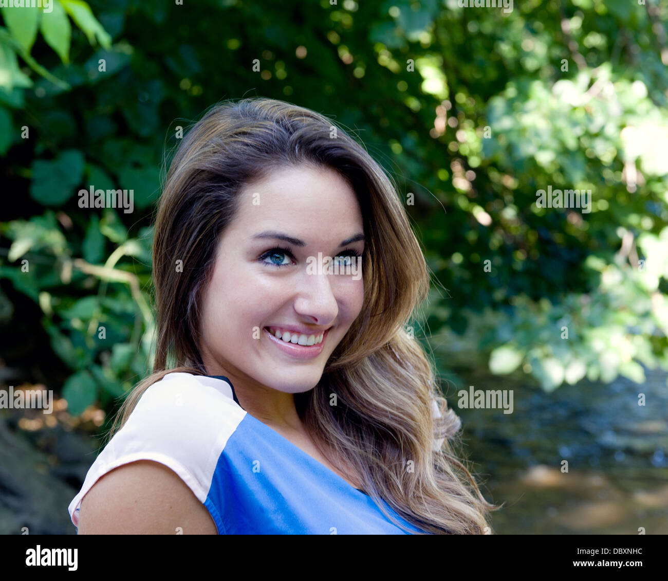 Kopf und Schultern von einer attraktiven Frau lächelnd während draußen an einem Sommertag. Stockfoto
