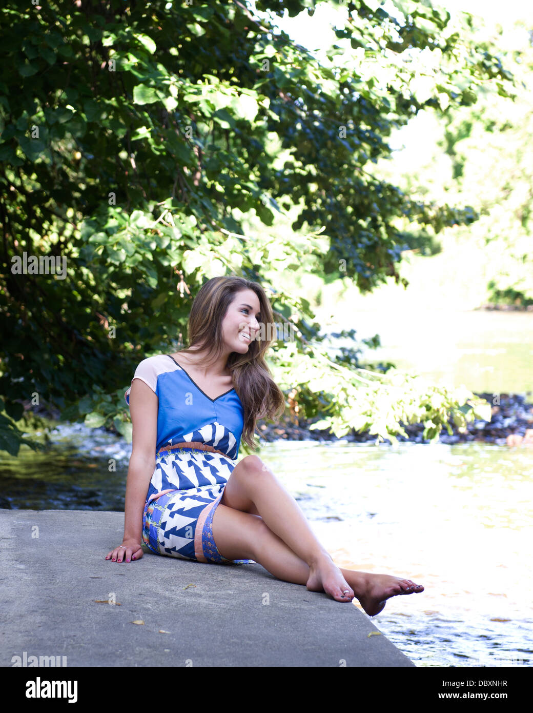 Junge Frau sitzt an einem Sommertag am Fluss außerhalb Stockfoto