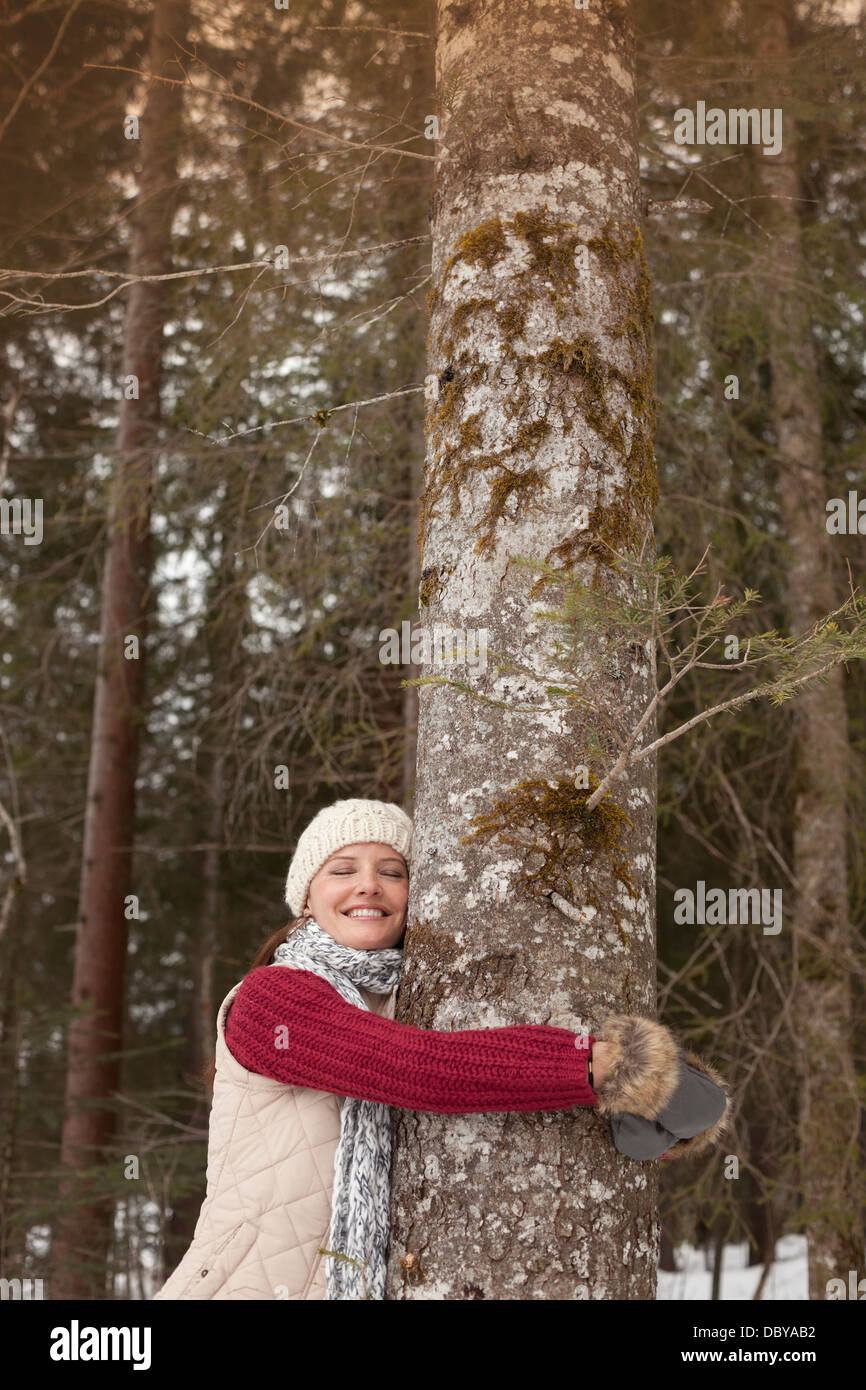 Glückliche Frau umarmt Baumstamm im Wald Stockfoto