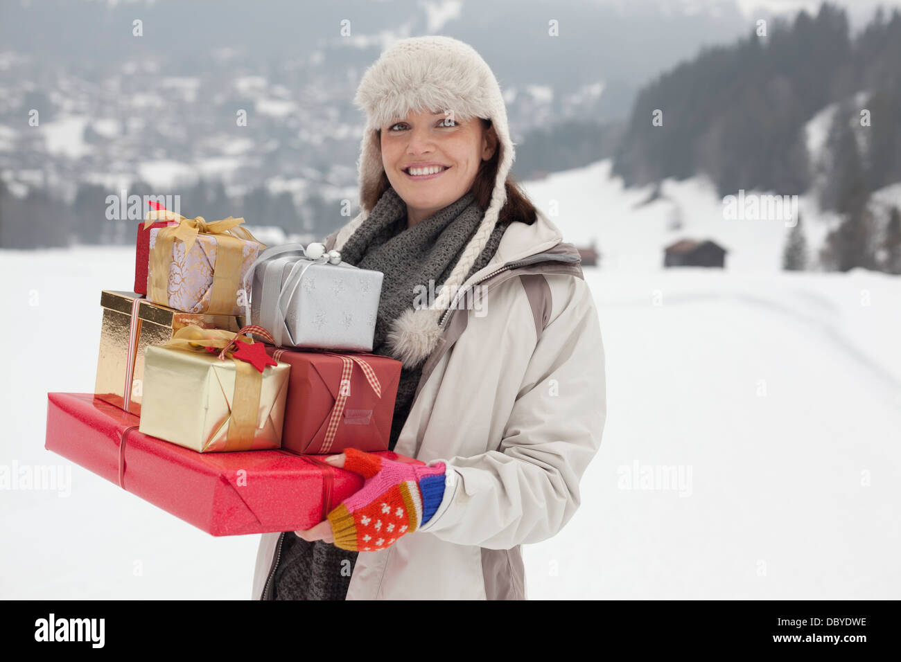 Porträt der lächelnde Frau, die Weihnachtsgeschenke in schneebedecktes Feld Stockfoto
