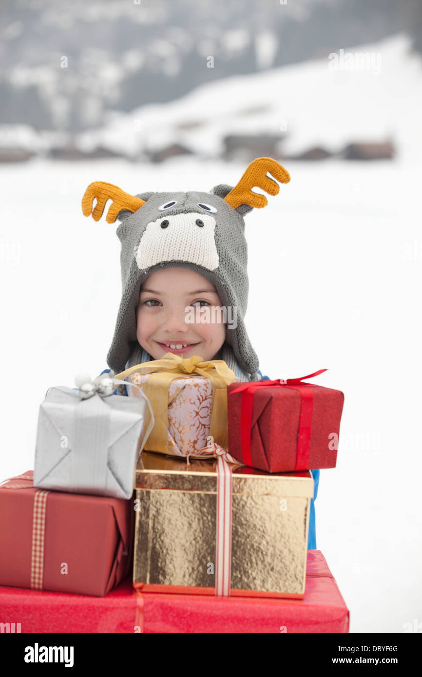 Porträt von lächelnden jungen Rentier Hut und Durchführung Stapel von Weihnachtsgeschenke im Schnee Stockfoto