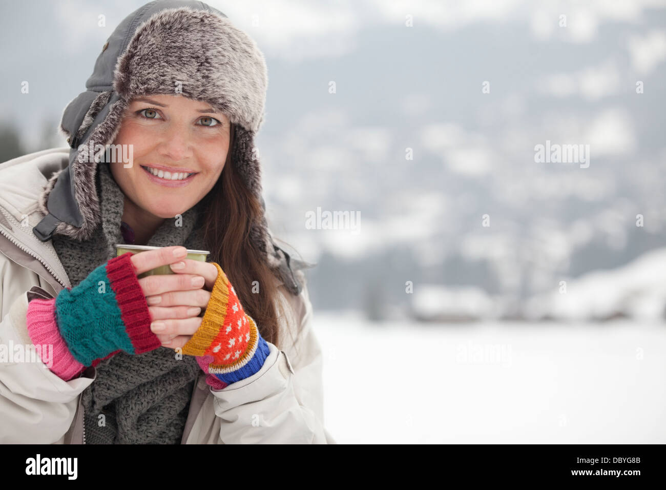 Porträt der glückliche Frau in Pelzmütze Kaffeetrinken in schneebedecktes Feld Stockfoto