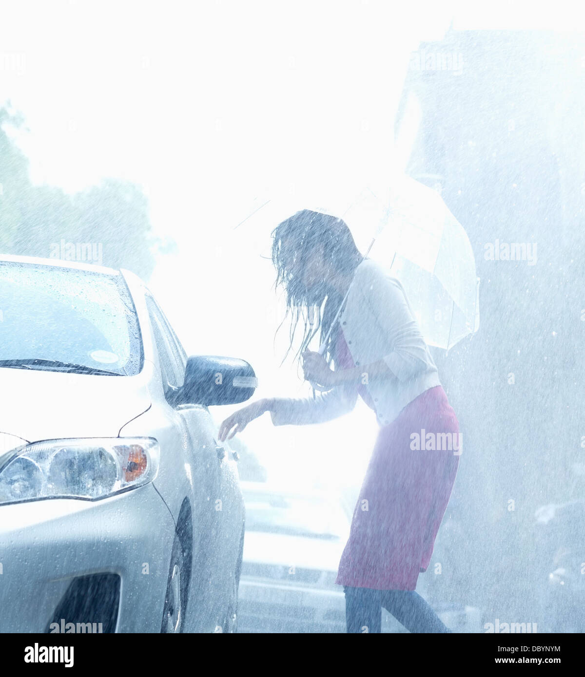 Frau mit Regenschirm für Auto Türgriff im Regen zu erreichen Stockfoto