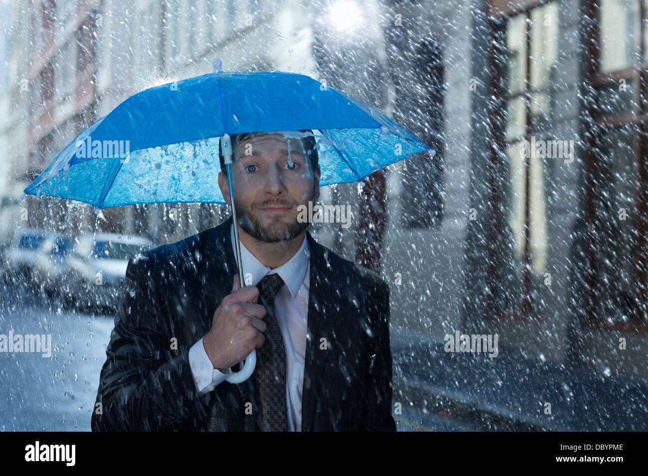 Porträt der Geschäftsmann mit winzigen Schirm im Regen Stockfoto