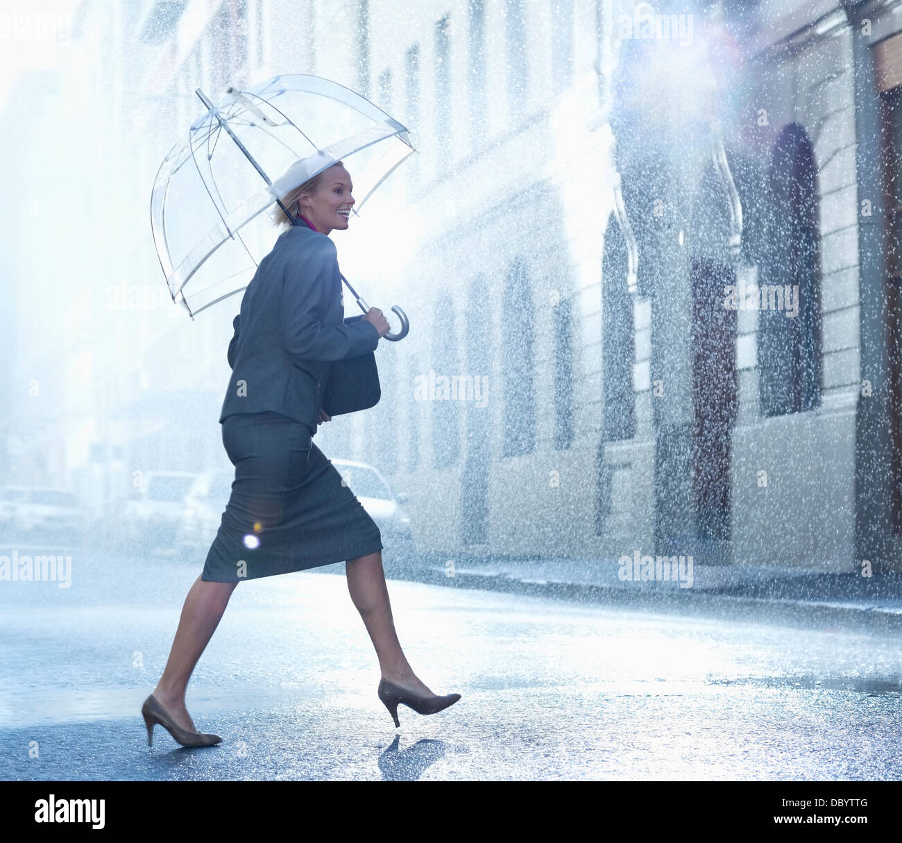 Glücklich Geschäftsfrau mit Regenschirm zu Fuß über die verregnete Straße Stockfoto