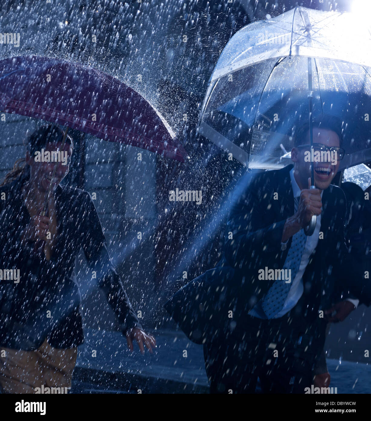 Glücklich Geschäftsleute mit Sonnenschirmen im Regen laufen Stockfoto