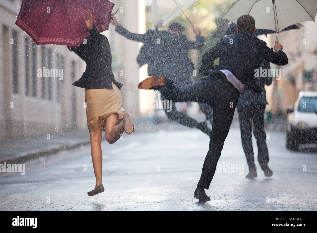 Geschäftsleute mit Sonnenschirmen, tanzen im Regen Stockfoto